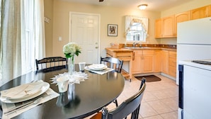 Un coin repas avec une table ronde dressée pour quatre personnes, un ventilateur de plafond et une cuisine en arrière-plan.