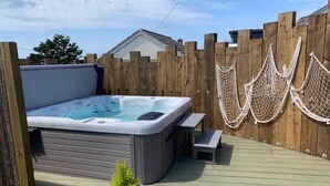 Un bain à remous avec une terrasse en bois, un petit banc et un hamac.