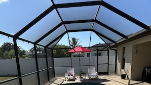 A covered swimming pool with inflatable swan and unicorn floats, a red umbrella, and a white fence in the background. - Come relax, restore and play at this calming fun retreat! Location! Pool, BBQ. (Cape Coral)