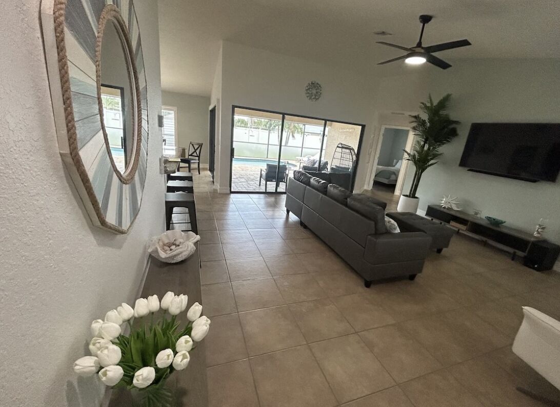 A spacious living room with a gray sofa, a television, and a ceiling fan.