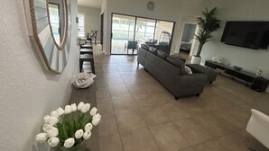 A spacious living room with a gray sofa, a television, and a ceiling fan. - Come relax, restore and play at this calming fun retreat! Location! Pool, BBQ. (Cape Coral)