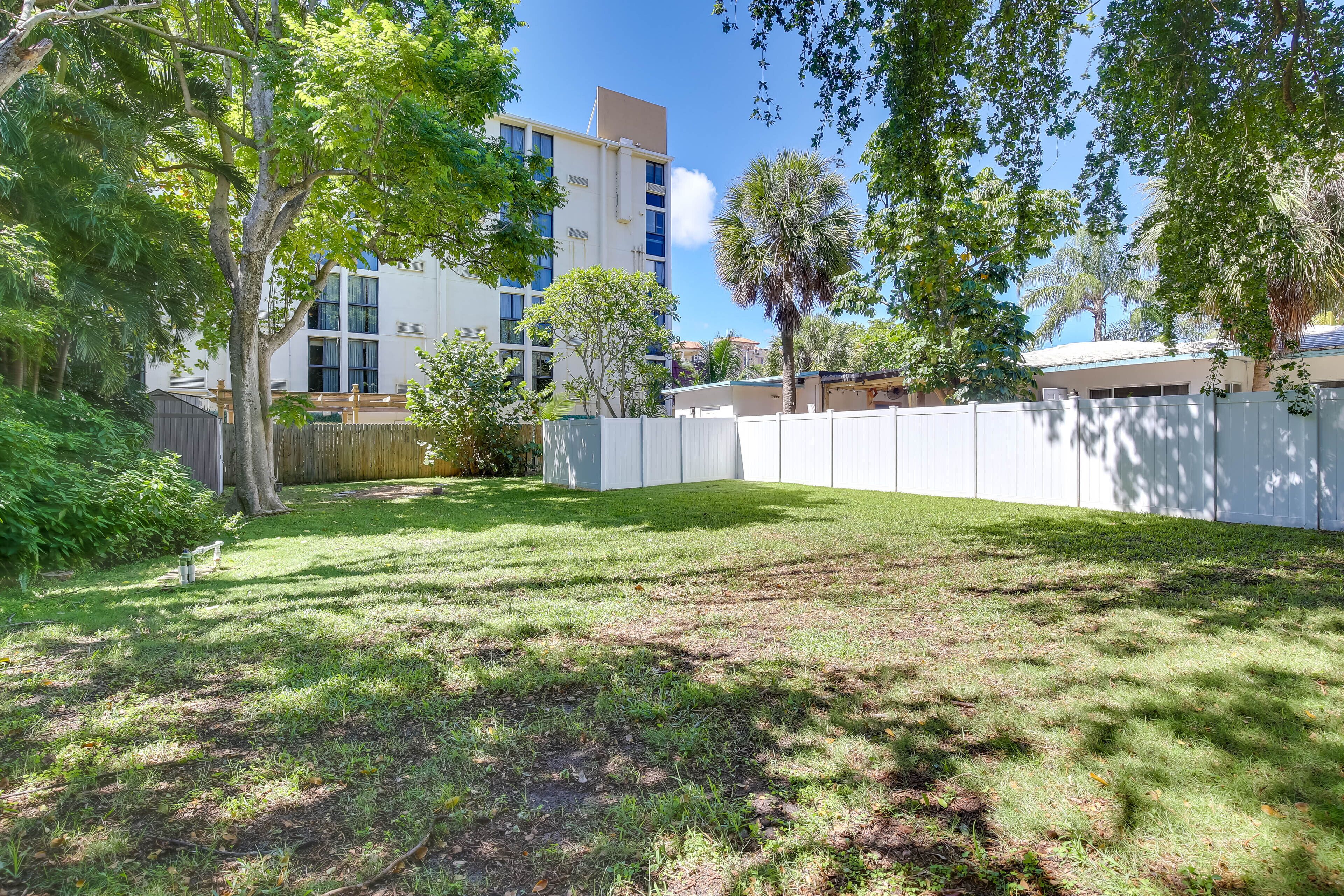 A grassy backyard with trees and a white fence.