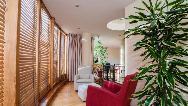 A modern living room with wooden blinds, a red armchair, a white sofa, and a potted plant. - ROOFTOP 3BR PH-INDOOR SAUNA IN DUBLIN (Dublin)