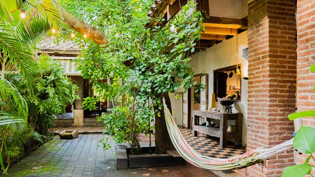 A brick-walled building with a checkered floor, a hammock, and lush greenery. - Hotel CRC-8S Cerca al Mar con Desayuno  (Cartagena)