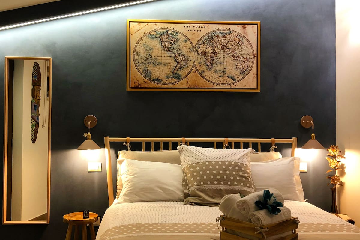 A bedroom with a bed, pillows, a wooden headboard, a globe artwork, a nightstand, and a small table.