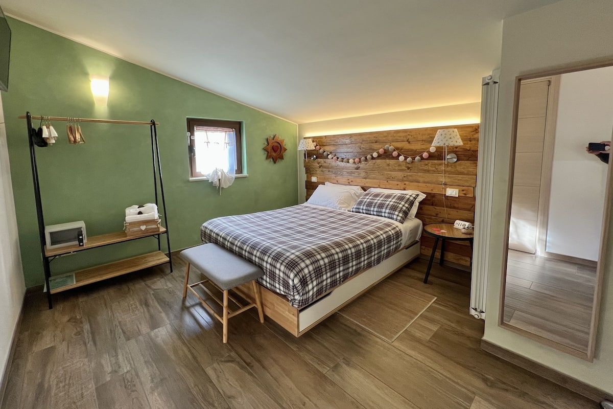 A bedroom with a bed, bench, bedside table, lamp, and a window with curtains.