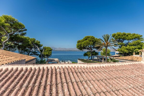 A terracotta-tiled roof overlooking a coastal view with trees and a clear blue sky. - Villa Me Chabot (Alcúdia)