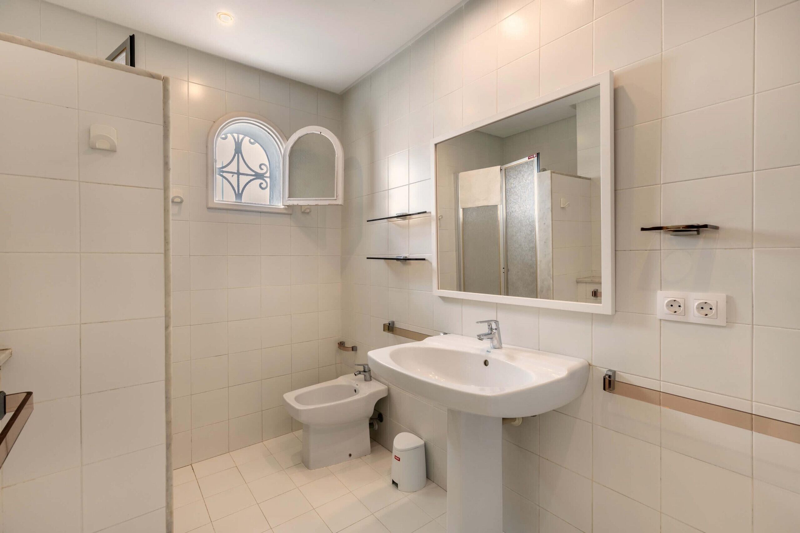 Ein modernes Badezimmer mit einem weißen Waschbecken, einem Bidet und einem kleinen Fenster mit dekorierter Scheibe.