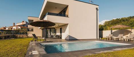 A modern two-story house with a swimming pool, outdoor seating, and a clear sky.