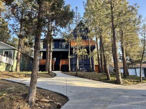 A modern two-story building with a dark exterior and wooden accents, surrounded by tall pine trees.