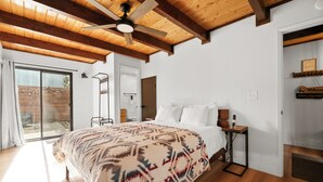 Un dormitorio con cama, vigas de madera en el techo, ventilador de techo, mesita de noche y puerta que da a un balcón.