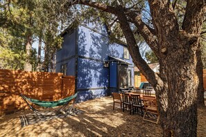 A blue cabin with a patio area, including a hammock, chairs, and a table.