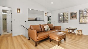 Una sala de estar moderna con un sofá de cuero marrón, piso de madera, una mesa de centro de vidrio y una pequeña mesa con sillas.