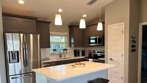 A modern kitchen with stainless steel appliances, a central island, pendant lighting, and a view of the outdoors. - Waterfront Gem, kayak, fish, restaurants close by (Port Charlotte)