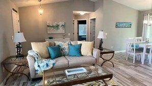 A living room with a sofa, coffee table, and lamps. There is a dining area with chairs and a table. - Waterfront Gem, kayak, fish, restaurants close by (Port Charlotte)