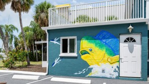 Un bâtiment orné d’une fresque représentant un poisson, avec une porte blanche et un balcon.