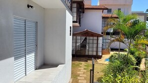 Ein überdachter Außenbereich mit Fliesenboden, einem Metallgitter und einem kleinen Garten mit Pflanzen und einer Palme.