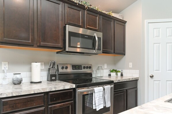 A modern kitchen with dark wood cabinets, stainless steel appliances, and a marble countertop. - Comfortable 3 bed 2 bath home in Nampa - Sleeps 6 (Nampa)