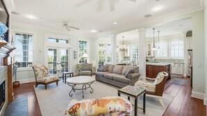 A spacious living room with a fireplace, a dining area, and a kitchen with large windows. - 108 Davis Love Drive (Fripp Island)