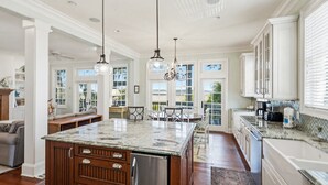 A spacious kitchen with a central island, wooden cabinetry, and a dining area with a view. - 108 Davis Love Drive (Fripp Island)