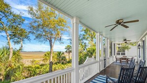 A covered porch with a view of a beach and palm trees, wooden chairs, and ceiling fans. - 108 Davis Love Drive (Fripp Island)