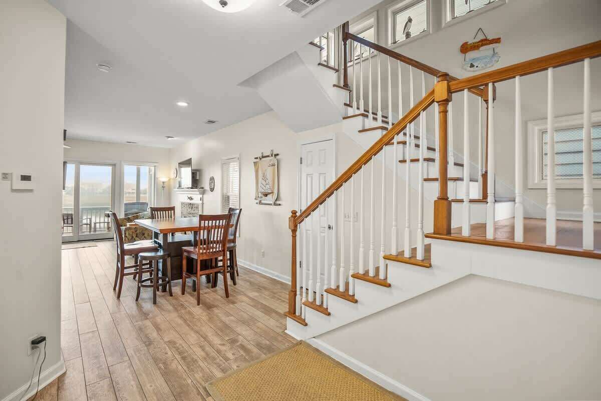 A spacious dining area with a wooden table and chairs, a staircase with white railings, and a view to a balcony.
