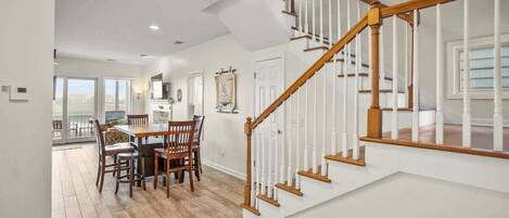 A spacious dining area with a wooden table and chairs, a staircase with white railings, and a view to a balcony.
