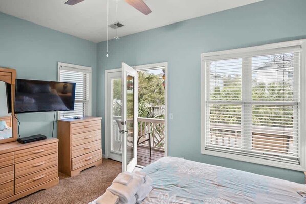 Un dormitorio con cama, cómoda, televisor y balcón con vista a follaje.
