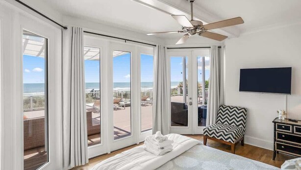 A bedroom with a bed, a chair, a TV, and a balcony with a view of the ocean.