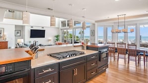 A modern kitchen with a large island, built-in appliances, and a dining area with wooden chairs.