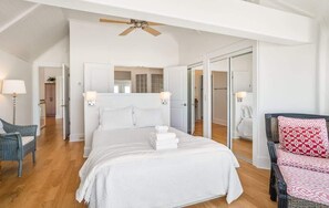 Une chambre avec un grand lit, un ventilateur de plafond, un miroir et une chaise.