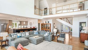 A spacious living area with a large grey sectional sofa, a wooden dining table, and a kitchen in the background.
