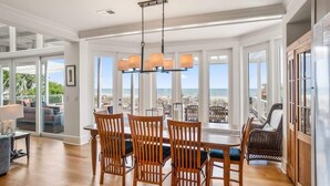 A dining area with a view of the ocean, wooden chairs, and a hanging light fixture.