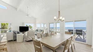 A spacious living area with a large wooden dining table, comfortable seating, a flat-screen TV, and a balcony with a view of the ocean. - 446 Tarpon Blvd (Fripp Island)