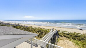 A beach view from a wooden deck with a white railing, leading to a sandy beach with waves, and a clear blue sky. - 446 Tarpon Blvd (Fripp Island)