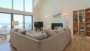 A living room with a large window, a fireplace, a television, and a bookshelf. - 458 Tarpon Blvd (Fripp Island)