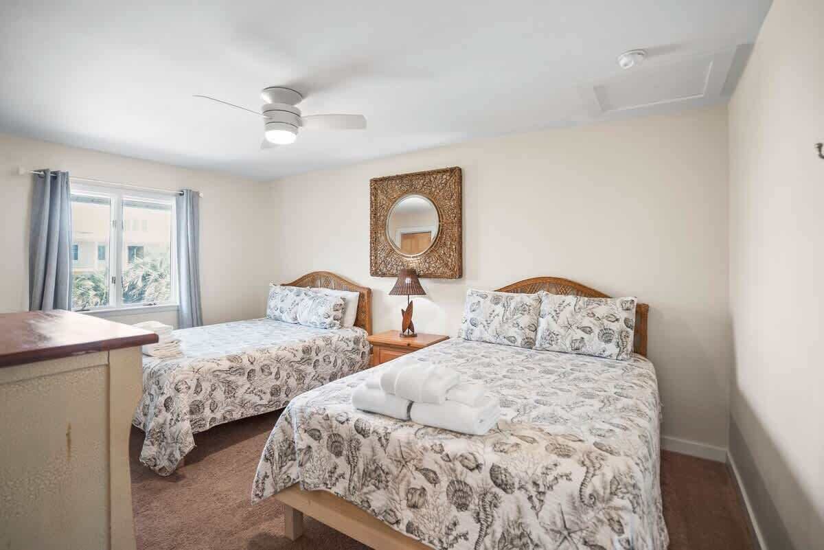A bedroom with two beds, a ceiling fan, a mirror, and a window with curtains.