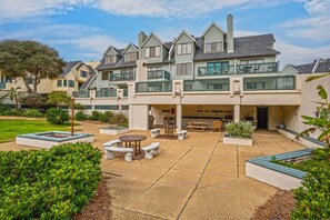 Um edifício residencial com vários andares, área de pátio, mobiliário de jardim e um jardim ajardinado.