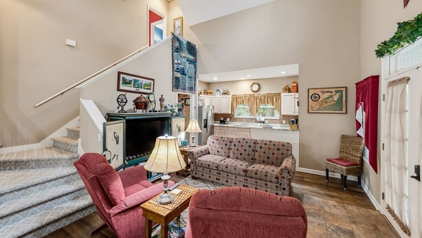 A spacious living area with a staircase leading to a kitchen, featuring a fireplace, patterned sofas, and a dining table. - 23 Davis Love Drive (Fripp Island)