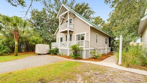 A two-story house with a covered porch, surrounded by lush greenery and a gravel driveway. - 23 Davis Love Drive (Fripp Island)