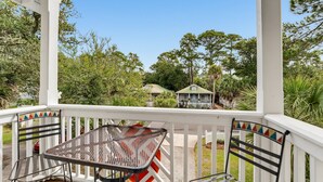 A covered porch with a table and chairs, overlooking a residential area with trees and a house. - 23 Davis Love Drive (Fripp Island)