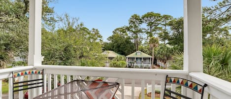 A covered porch with a table and chairs, overlooking a residential area with trees and a house.