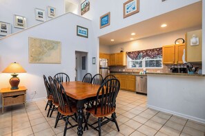 Un coin repas avec une table et des chaises en bois, une carte accrochée au mur, et une cuisine dotée de meubles en bois et d’une fenêtre.