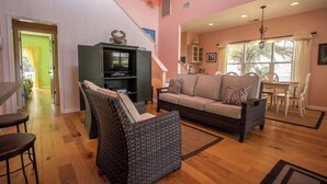 Un salon comprenant un canapé, deux fauteuils, un téléviseur et un coin repas avec une table et des chaises.
