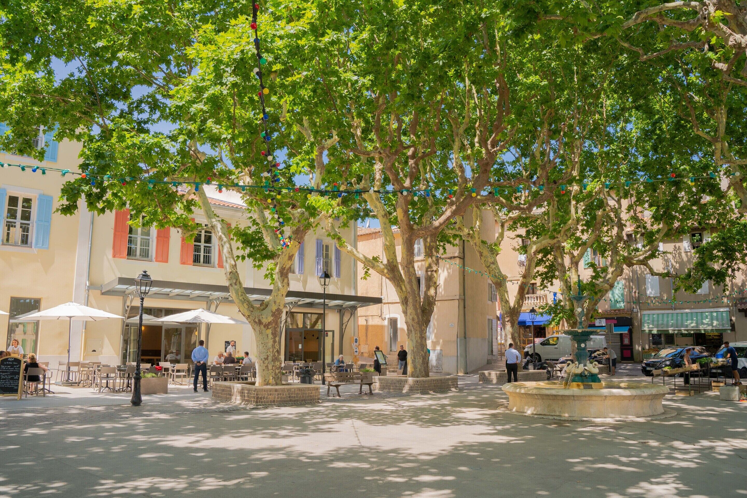 Un espace de café en plein air, avec des tables et des chaises, entouré d’arbres et de bâtiments.