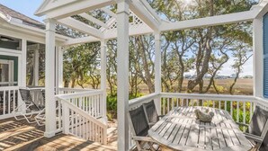 Un espace extérieur abrité, doté d’une table et de chaises en bois, de rampes blanches et offrant une vue sur les arbres et un paysage ouvert.