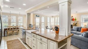 Una cocina amplia con una isla central, armarios blancos y una zona de comedor con mesa y sillas de madera.