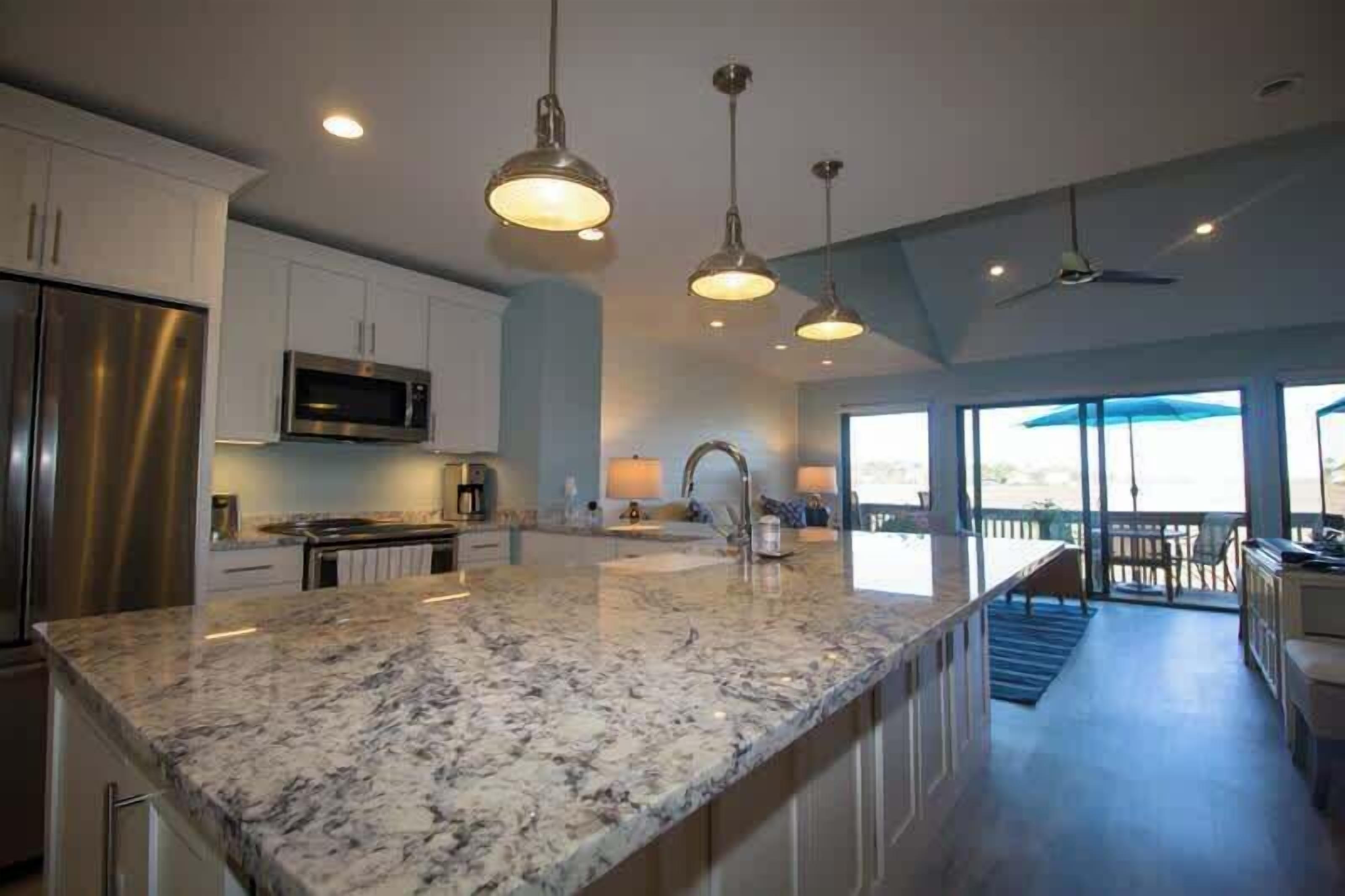 A modern kitchen with granite countertops, stainless steel appliances, pendant lighting, and a view to the outside.