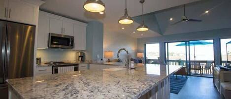 A modern kitchen with granite countertops, stainless steel appliances, pendant lighting, and a view to the outside.
