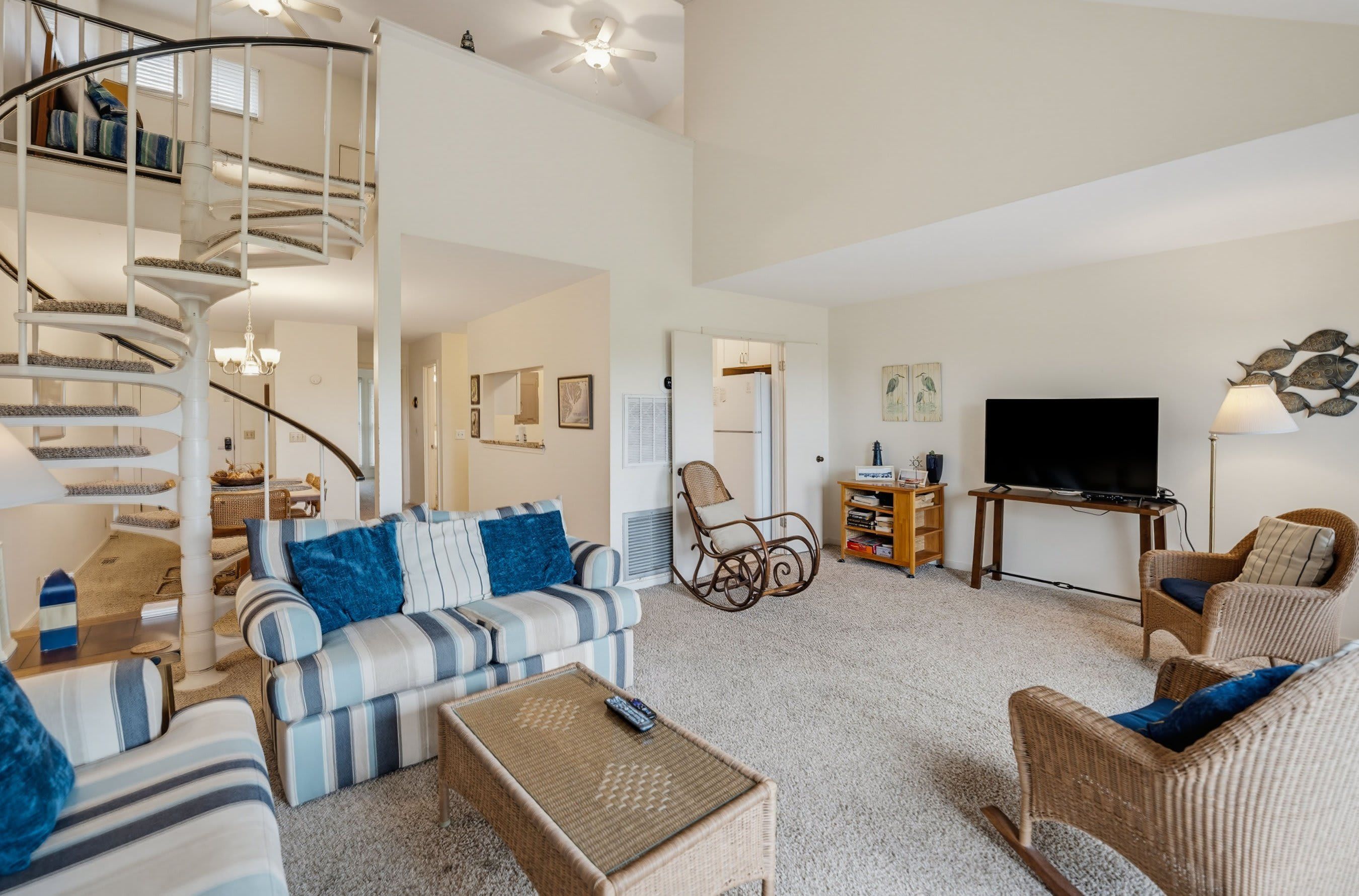 A spacious living room with a spiral staircase, a sofa set, a television, and a dining area.